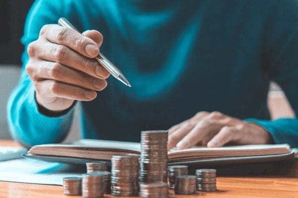 Pessoa faz anotações ao lado de pilhas de moedas